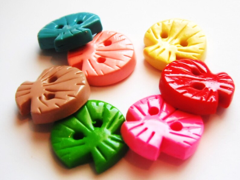 May include: Assortment of colorful plastic buttons shaped like leaves. The buttons are in shades of green, pink, red, brown, yellow, and blue.