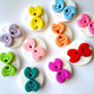 May include: Ten colorful buttons with a butterfly design. Each button has a white background with a raised butterfly design in a different color. The colors include pink, red, orange, yellow, green, blue, purple, and teal.