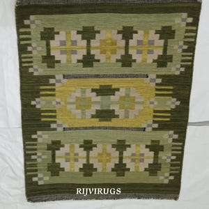 May include: A rectangular green rug with a geometric pattern in shades of green, yellow, and gray. The rug features a central design and repeating motifs. The text "RIJVIRUGS" is visible at the bottom.