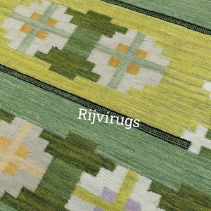 May include: Close-up of a green and yellow patterned rug with the text "Rijvirugs". The rug features repeating floral-like designs in shades of green, yellow, white, and purple. The rug has a textured appearance.