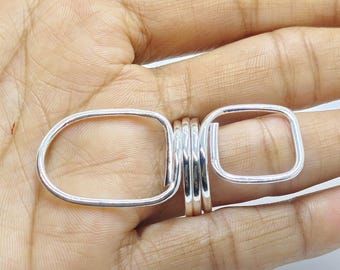 May include: A silver-colored ring featuring a multi-coil band design. The ring has two distinct geometric shapes extending from the central coiled section: one side forms a large, rounded oval loop, while the other side forms a smaller, square-like loop.
