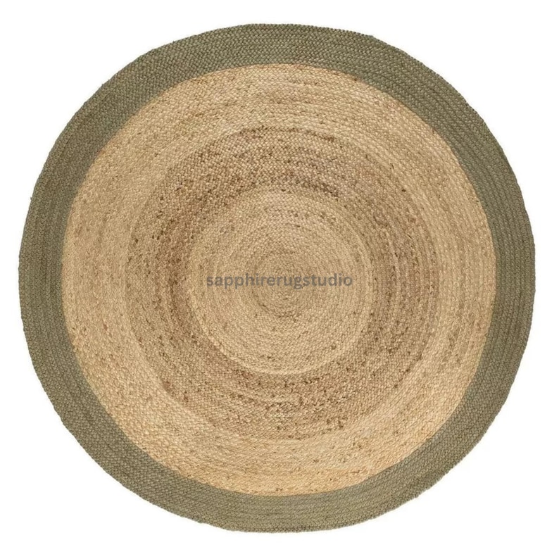 May include: A round jute rug with a natural tan center and a sage green border. The rug has a woven texture and a circular design, suitable for a living room or bedroom. The rug's diameter is approximately 60 inches.