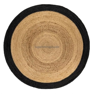 May include: Round jute rug with a black border. The rug features concentric circles of natural jute tones, creating a textured surface. The black border provides a contrasting edge to the neutral tones of the rug. The rug is suitable for indoor use.