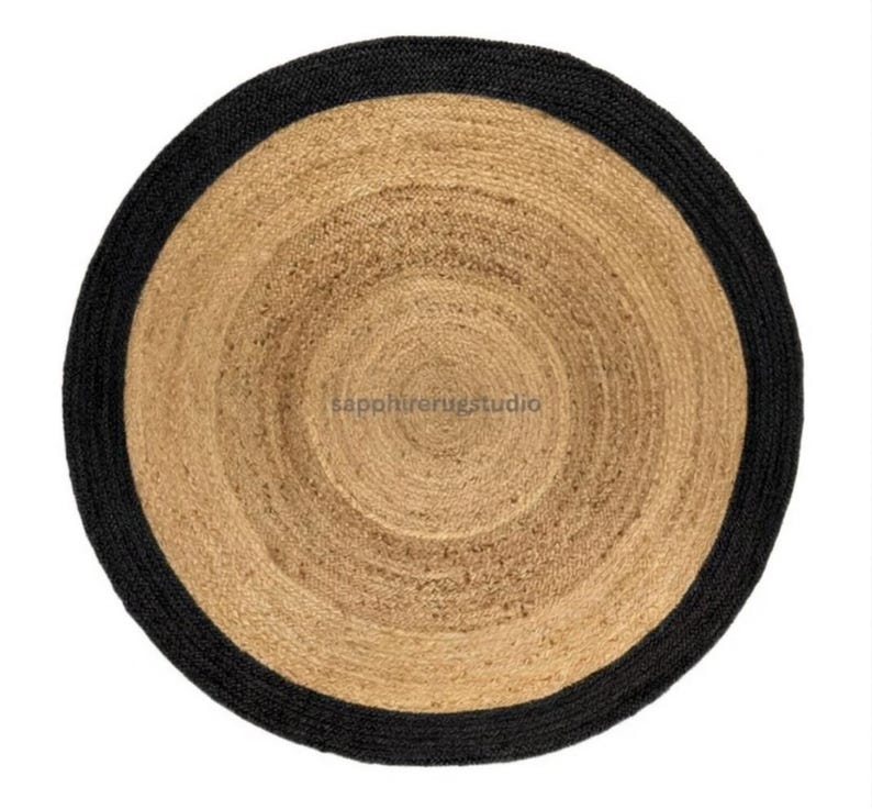 May include: Round jute rug with a black border. The rug features concentric circles of natural jute tones, creating a textured surface. The black border provides a contrasting edge to the neutral tones of the rug. The rug is suitable for indoor use.