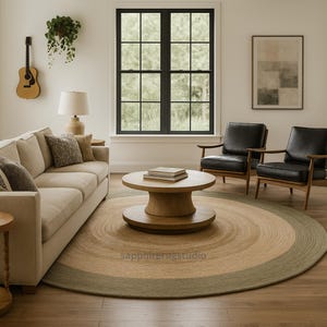May include: A round jute rug with a concentric design in shades of tan and green. The rug is in a living room setting with a sofa, chairs, and a wooden coffee table. The room has a neutral color palette.