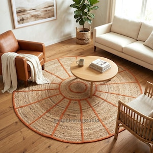 May include: A round jute rug with an orange geometric design. The rug is placed in a living room with a brown leather armchair, a light-colored sofa, and a wooden coffee table. The rug's diameter is approximately 7 feet.