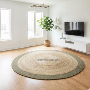 May include: A round jute rug with a natural beige center, a light green border, and a braided texture. The rug is in a modern living room with a plant and a television. The text "sapphirerugstudio" is visible on the rug.