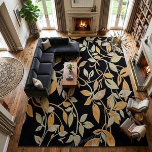 May include: An overhead view of a living room featuring a large black rug with a botanical leaf design in shades of gold and cream. A dark gray sectional sofa, a wooden coffee table, and a round rug are also visible.