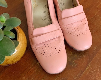 Pode incluir: Um par de sapatos de couro rosa com um design perfurado e uma tira na parte superior. Os sapatos têm uma etiqueta dourada que diz "Fashion Ease" no interior.