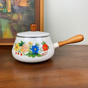 Peut inclure: Une casserole en émail blanc avec une poignée en bois et un motif floral avec des fleurs jaunes, rouges, bleues et vertes.