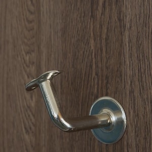 Può includere: Una maniglia per porta cromata lucida con un design curvo, montata su una porta in legno marrone scuro. La maniglia ha una base circolare e una leva curva, offrendo un'estetica elegante e moderna.