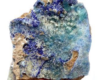 May include: A natural mineral specimen featuring a striking combination of colors. The piece showcases deep blue azurite crystals, light blue-green crystals, and a tan matrix. The mineral has a rough, textured surface and is an eye-catching display piece.