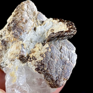 May include: Close-up of a mineral specimen featuring a cluster of crystals. The specimen displays a mix of colors, including brown, tan, and clear. The texture is rough and crystalline, with visible layers and formations. The background is black.