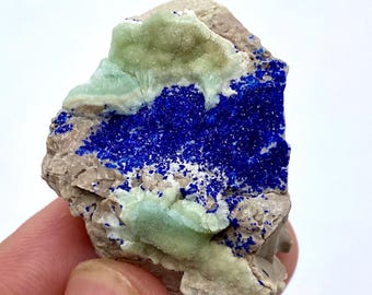 May include: A natural mineral specimen featuring a vibrant display of colors. The piece showcases a deep blue azurite formation, complemented by light green malachite and set within a matrix of beige rock. A unique geological find.