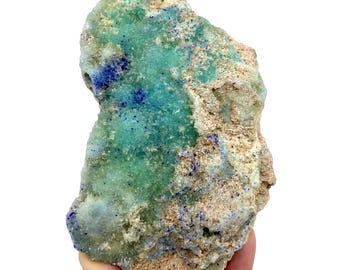 May include: A natural mineral specimen featuring a mix of colors. The stone has a light brown base with patches of vibrant turquoise and deep blue crystalline formations. The overall texture appears rough and uneven.