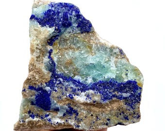 May include: A raw mineral specimen featuring a mix of colors. The stone has a base of tan and light green hues, with striking veins of deep blue azurite. The rough texture and natural form are clearly visible.