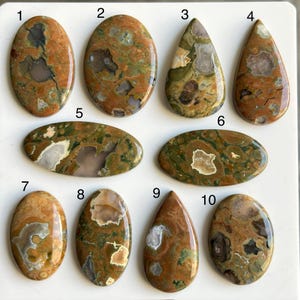 May include: A collection of ten polished gemstone cabochons in various shapes, including oval and teardrop. The stones feature a mix of earthy tones, with brown, green, and cream colors. Each stone has unique patterns and textures, suitable for jewelry making or collecting.