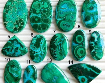 Può includere: Una collezione di quattordici pietre preziose di malachite lucidata in varie forme, tra cui ovali, triangoli e gocce. Le pietre mostrano una vibrante miscela di tonalità verde scuro e turchese, con motivi a vortice unici. Le pietre preziose sono disposte su una superficie bianca.