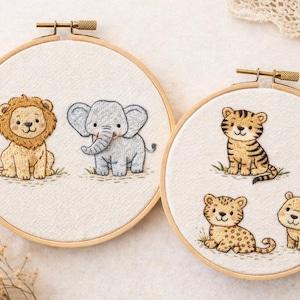 Könnte beinhalten: Zwei Stickrahmen mit niedlichen Tiermotiven. Einer zeigt einen Löwen und einen Elefanten, der andere einen Tiger, einen Leoparden und einen Bären. Jedes Tier ist in sanften Farben auf weißem Stoff gestickt, gefasst in einem Holzrahmen.