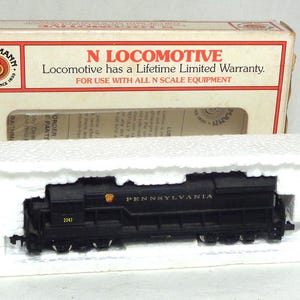 May include: A black N scale model locomotive, labeled "PENNSYLVANIA" with the number "2243", sits in a white foam insert within its original box. The box features the "BACHMANN" logo and text stating "N LOCOMOTIVE" and a lifetime warranty.