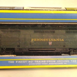May include: A green model train locomotive with "PENNSYLVANIA" printed on the side. The box is blue and yellow and says "AHM" and "The Finest HO Trains From Around The World."