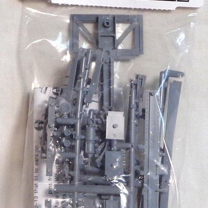 May include: A gray plastic model train tank car underframe kit. The package includes various small parts for assembly, with the text "TANK CAR UNDERFRAME" and "1 KIT HO SCALE".