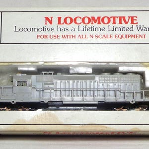 May include: A gray N scale locomotive model in a clear plastic case, inside a white cardboard box. The box has the Bachmann logo and text that reads "N LOCOMOTIVE" and "Locomotive has a Lifetime Limited Warranty."