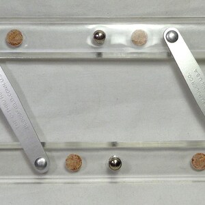 May include: A clear acrylic parallel ruler featuring two horizontal bars connected by two diagonal metal arms. The metal arms are engraved with the text FAIRGATE RULE CO. COLD SPRING N.Y. U.S.A. and include small cork and metal accents.