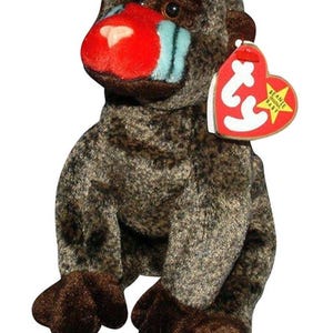 May include: A plush toy of a mandrill monkey with brown and gray fur. The monkey has a red nose, blue cheek stripes, and a tag that reads "Beanie Baby". The toy is in a sitting position.