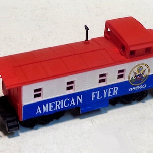 Könnte beinhalten: Ein roter, weißer und blauer Spielzeug-Güterwagen mit den Worten "AMERICAN FLYER" und der Nummer "98503" auf der Seite. Der Güterwagen hat ein kleines, rotes Dach mit einem schwarzen Schornstein.