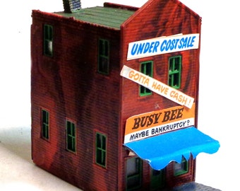 Puede incluir: Un edificio de ladrillo rojo con un techo verde y un toldo azul. El edificio tiene varias ventanas y un letrero que dice "Busy Bee Maybe Bankruptcy?"  El letrero está sobre otro letrero que dice "Under Cost Sale Gotta Have Cash!"