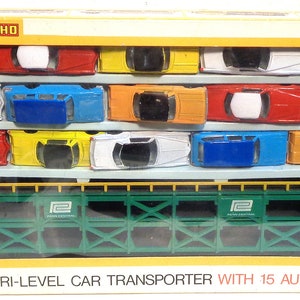 May include: A toy train car transporter with a green metal frame and 15 toy cars in various colors. The box reads "89' Tri-Level Car Transporter with 15 Autos".