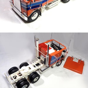 Può includere: Un modello dettagliato di un autoarticolato arancione e blu. La cabina presenta finiture cromate, un tetto bianco e strisce blu e bianche. Il camion ha più ruote e un sottocarro dettagliato.