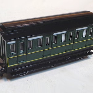 May include: A green and black toy train car with a black roof and windows. The car has a yellow stripe along the bottom.