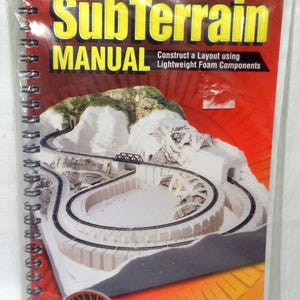 May include: A spiral-bound SubTerrain Manual by Woodland Scenics in a clear plastic sleeve. The cover features a model train layout with white foam terrain, black tracks, and a bridge. Text reads: SubTerrain MANUAL Construct a Layout using Lightweight Foam Components.