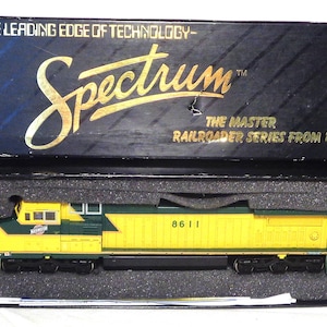 May include: A yellow and green model train locomotive, labeled "8611", sits in a black box. The box lid reads "Spectrum" and "The Master Railroader Series from Bachmann". The box is black with a blue top.