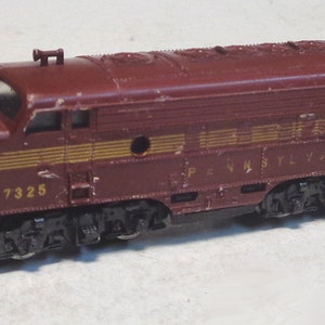 Puede incluir: Una locomotora de tren de juguete de color marrón con letras doradas que dicen "Pennsylvania" y el número "7325".