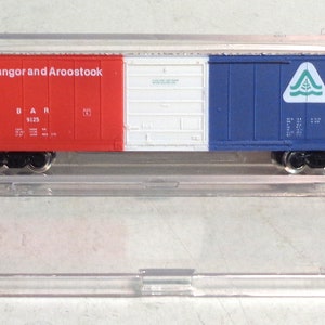 May include: A red, white, and blue model train boxcar with the words "Bangor and Aroostook" and "BAR 9123" printed on the side. The boxcar has a green triangle logo with a tree inside.
