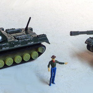 Puede incluir: Dos tanques militares de juguete, uno verde y otro verde oliva, con cañones y ruedas negras. Los tanques tienen marcas blancas que dicen "H8130".