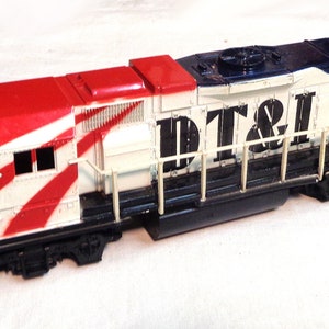 May include: A model train locomotive in red, white, and blue. The front of the model displays the number "1776", while the side features the letters "DT&I". The model is detailed with railings and other features.