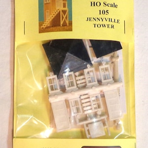 May include: A plastic model kit for an HO scale Jennyville Tower. The kit includes a tower, windows, and a roof. The packaging is yellow with a red and white logo for AM Models.