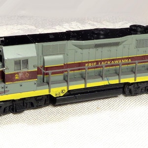 Puede incluir: Una locomotora de tren modelo en tonos grises, amarillos y granates. Las palabras "ERIE LACKAWANNA" están impresas en el lateral. El modelo tiene ruedas negras y un techo negro. El número "240" es visible en la parte delantera.