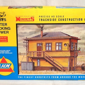 May include: A yellow box for a model railway kit, showing an illustration of an Interlocking Tower. The box includes the text "MINIKITS" and "TRACKSIDE CONSTRUCTION KITS". The model depicts a two-storey building with a staircase and architectural details.