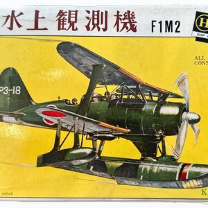 Puede incluir: Un kit de maqueta de un hidroavión Aichi E13A1 de la Armada Japonesa, también conocido como "Jake", con el texto "零式水上観測機 F1M2" y "P3-18" en la caja. La caja es amarilla con texto negro y una bandera japonesa roja y blanca.