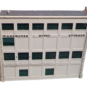 May include: A white model building with green windows and the text "WAREHOUSE - RUSSO - STORAGE" on the front.