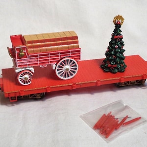 May include: A red toy train car with a red wagon carrying a stack of wooden blocks and a green Christmas tree with a gold star on top.