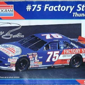 May include: A blue and red 1:24 scale model car kit of a Ford Thunderbird race car with the number 75 and the words "Factory Stores Outlet Centers" on the side. The car is a model of the car driven by driver,  'Yell Sellin'.