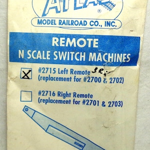 May include: A white paper packaging for Atlas Model Railroad Co., Inc. remote N scale switch machines. The text includes #2715 Left Remote and #2716 Right Remote, with an illustration of a switch machine and the company address in Hillside, NJ.