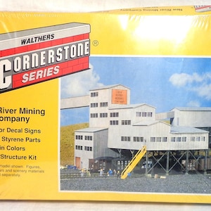 May include: A model kit for a New River Mining Company building. The kit is part of the Cornerstone Series by Walthers. The box shows a pre-production model of the building, which is a multi-level structure with a large sign that reads "New River Mining Company".