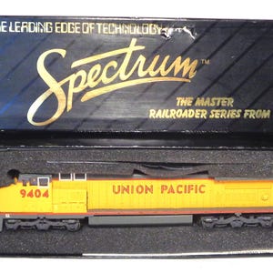 May include: A yellow and red Union Pacific model train locomotive, number 9404, is displayed in its original box. The box is black with the words "Spectrum" and "The Master Railroader Series From Bachmann" printed on it.